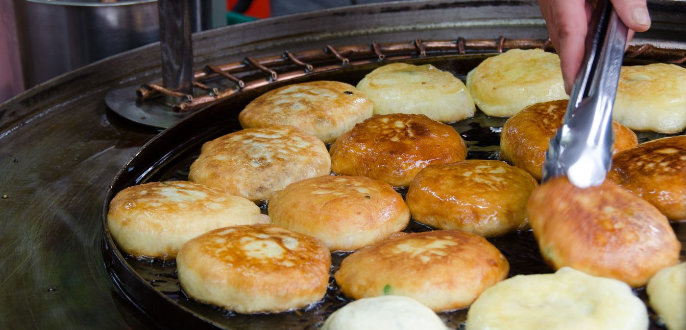 Hotteok being pressed flat on the griddle. The filling inside is molten sugar — it is served far hotter than it looks.
