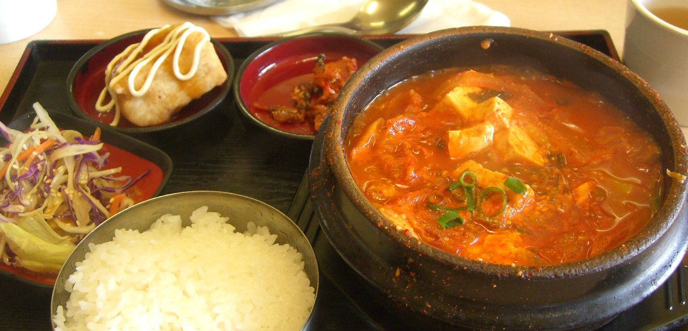 Kimchi-jjigae as it arrives: the pot, a steel bowl of rice, and side dishes nobody ordered.