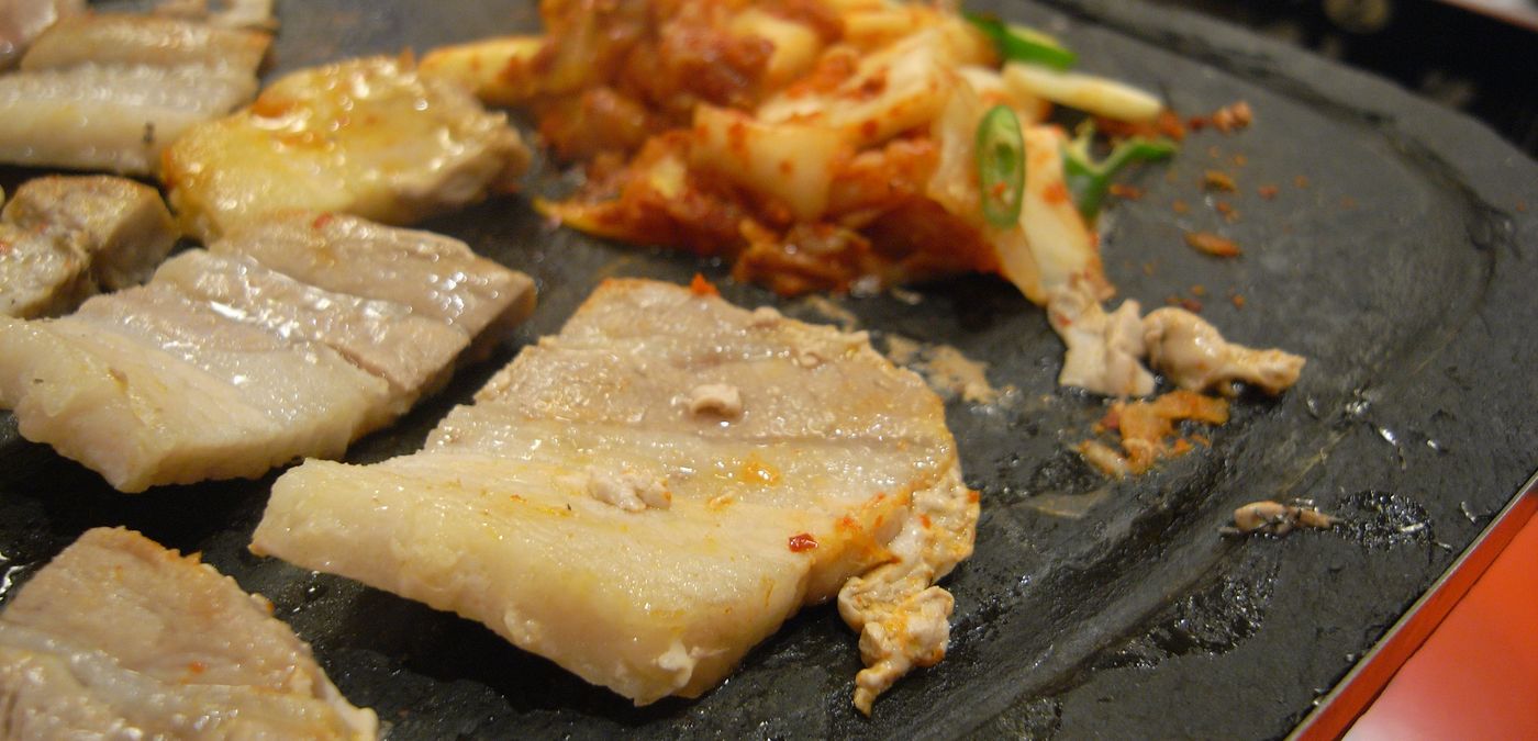 Samgyeopsal on the grill, with kimchi cooking beside it — the kimchi is meant to be eaten hot, off the same grill.