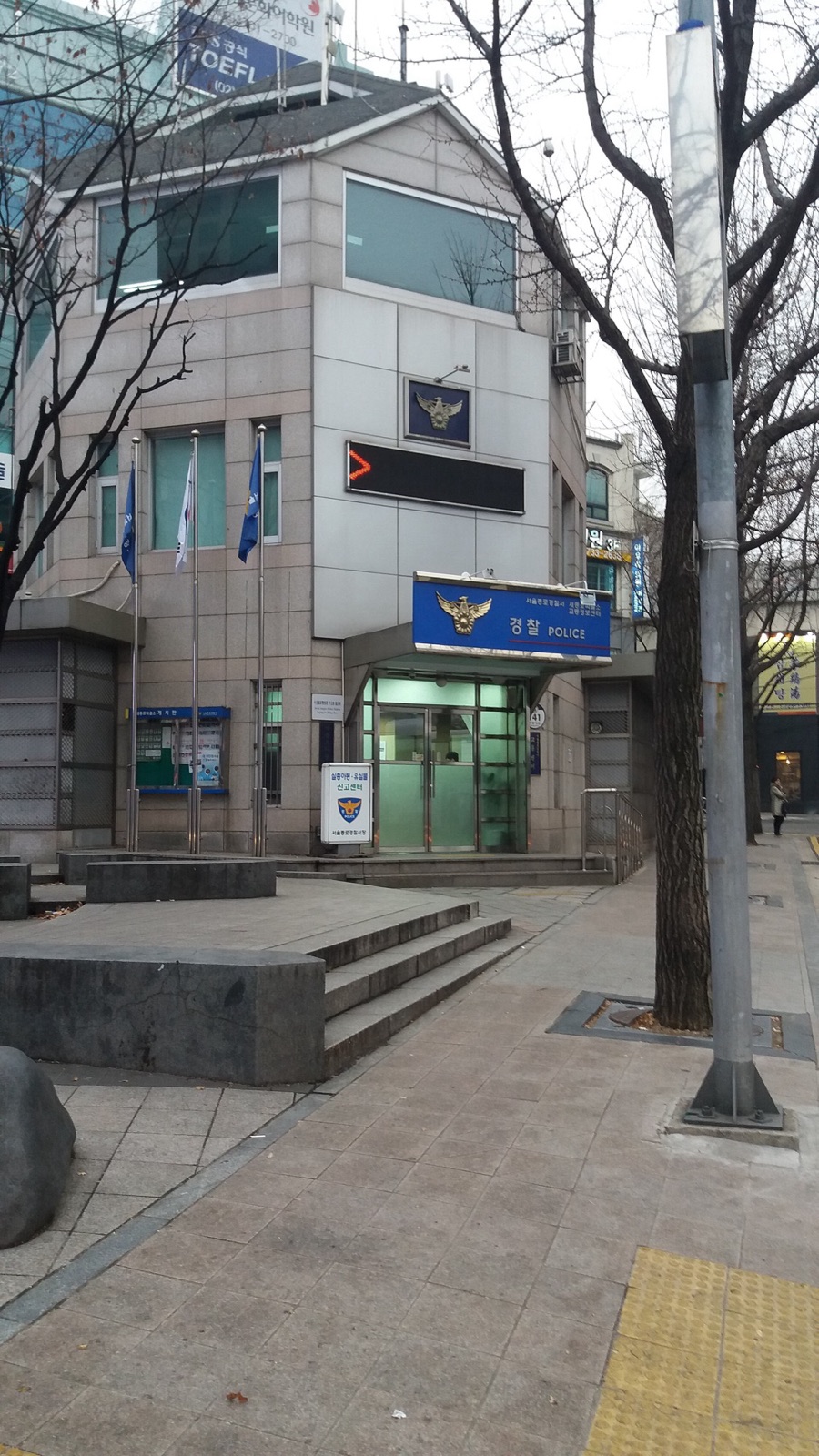 ソウル中心部の小さな派出所。ガラス扉の上に「경찰 POLICE」と書かれた青い看板があり、入口の横に白い案内板が立っている