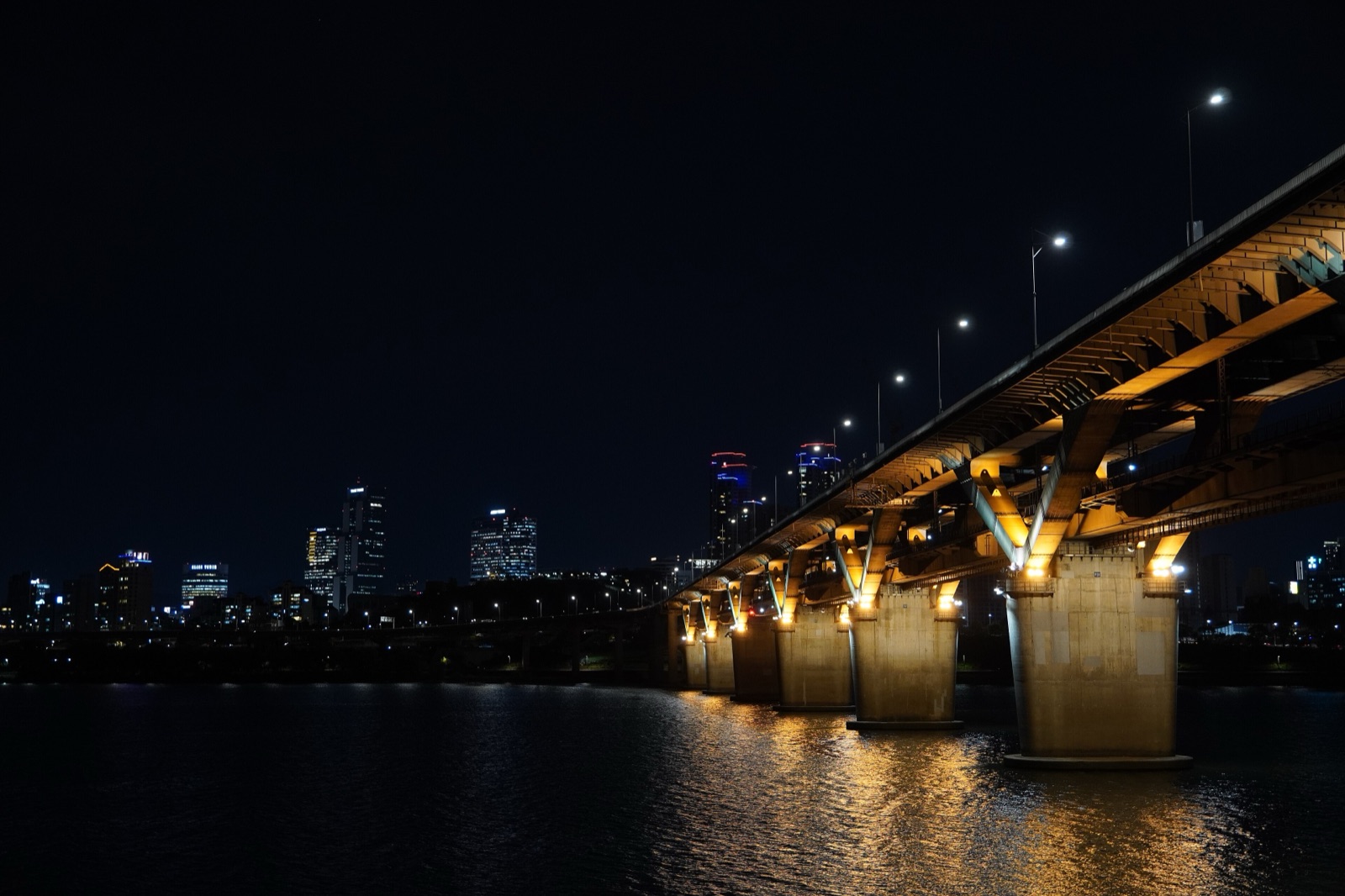 Cheongdam Bridge lit up in gold over the dark Han River at night, seen from Ttukseom Hangang Park in Seoul