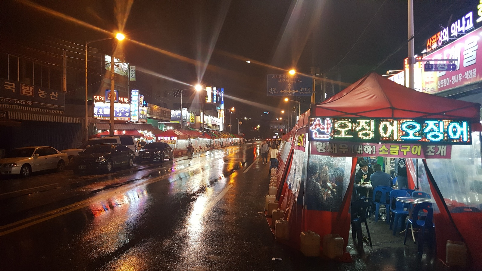 A row of red tented pojangmacha street stalls with lit signs along a wet street at night next to Chilseong Market in Daegu